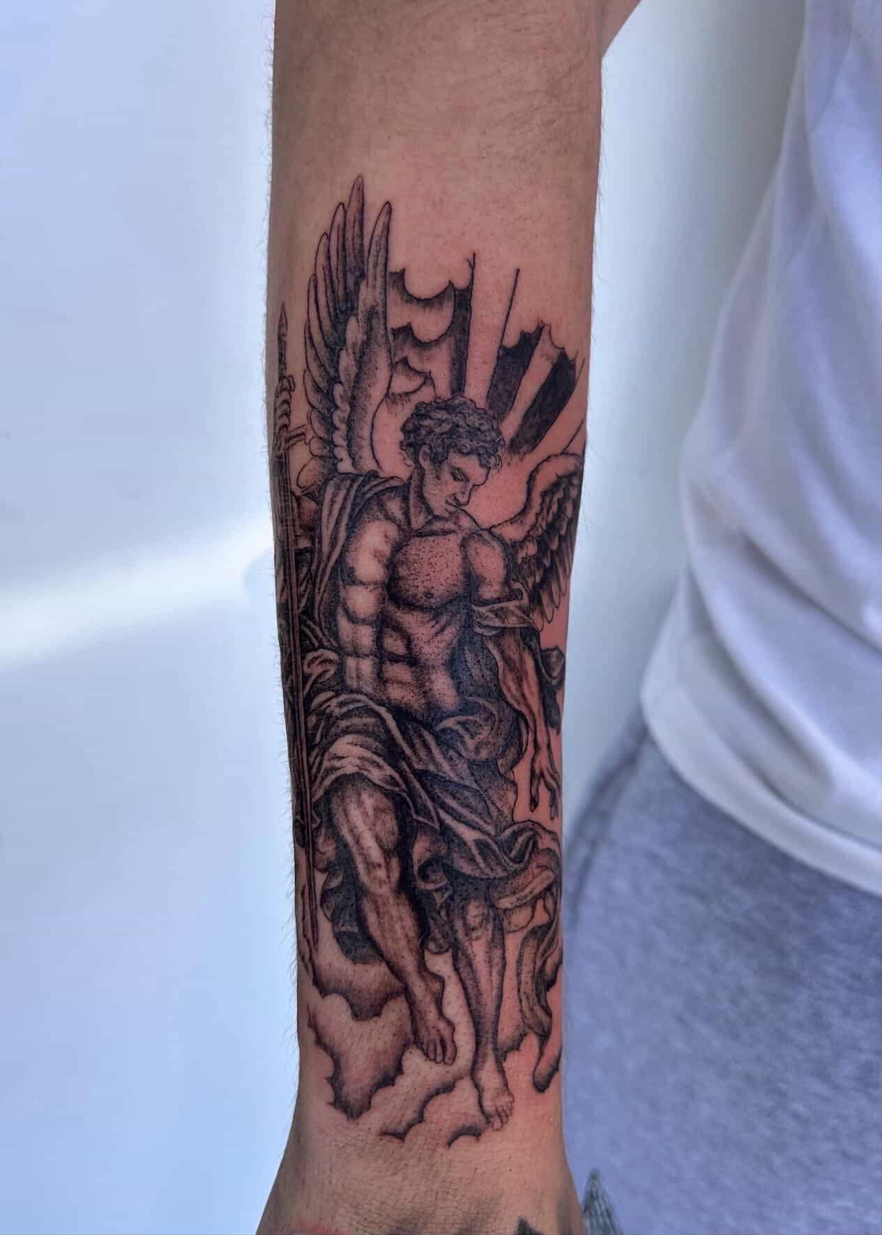 Black-and-grey realism dotwork angel figure with wings and spear on the forearm.