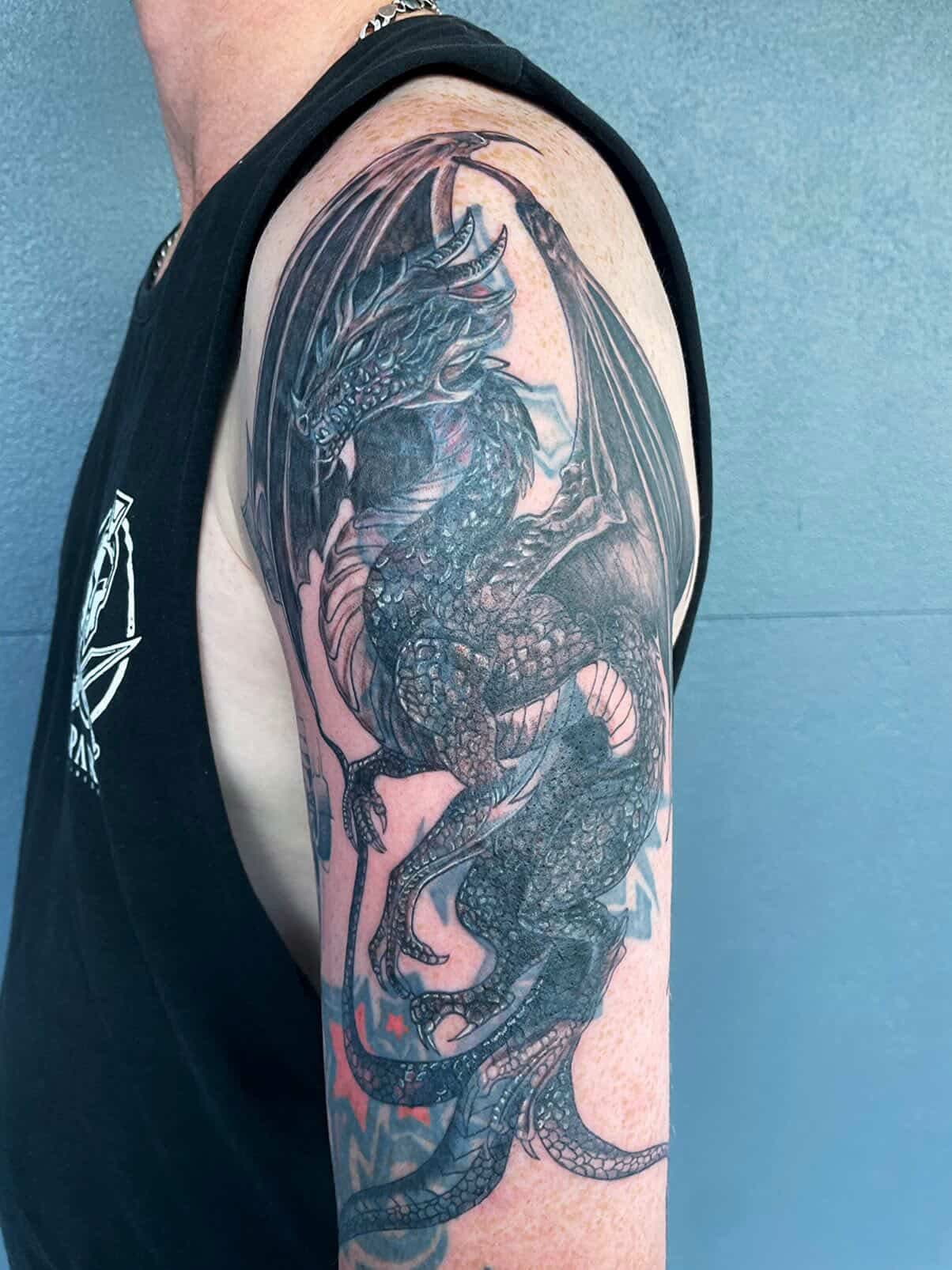 Detailed black-and-grey dragon sleeve tattoo with fine scale shading.
