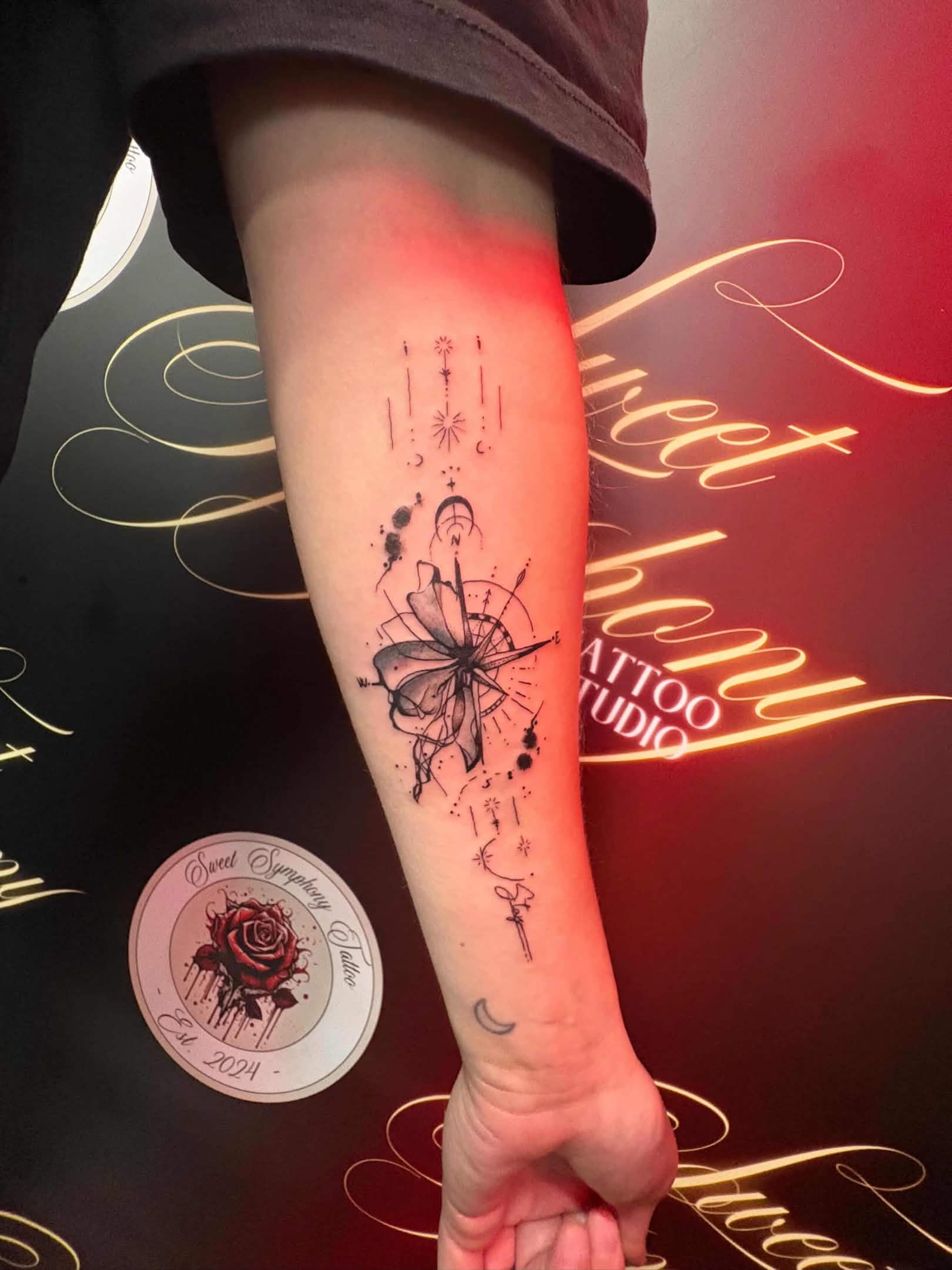 Minimalist fine-line celestial compass and flower tattoo running down the forearm.