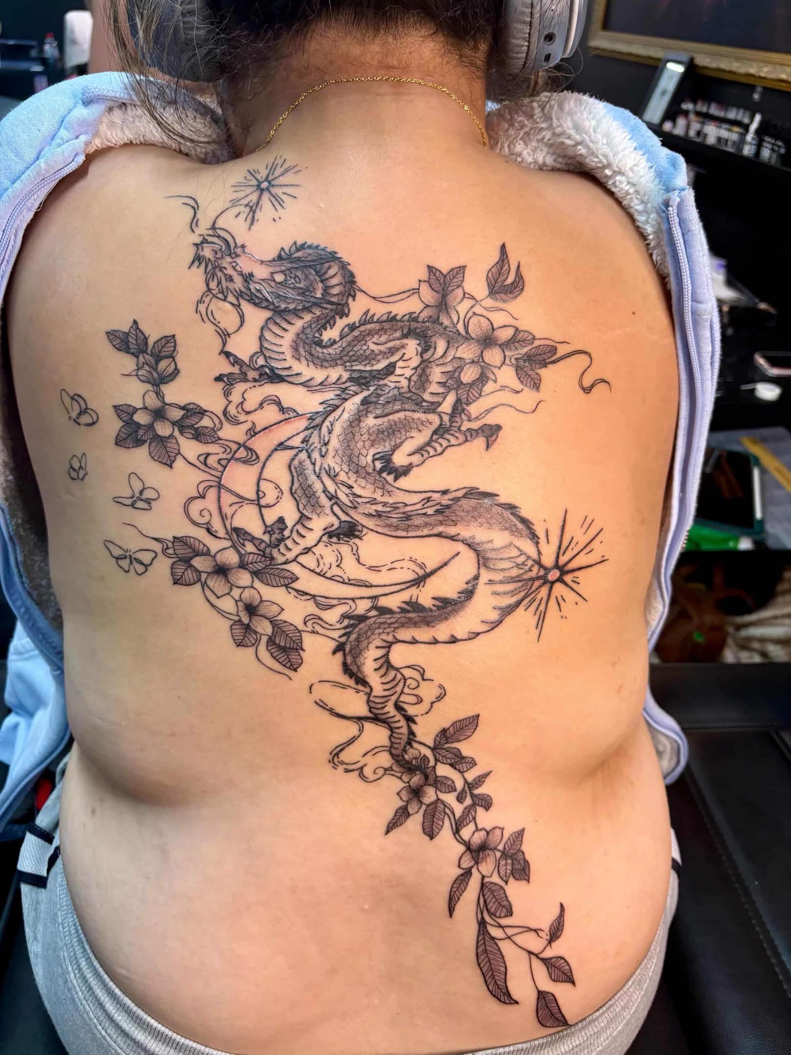Fine-line Asian-style dragon tattoo winding through cherry blossoms across the back.